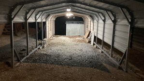 Un espace extérieur abrité, doté d’un sol en gravier, de poutres métalliques et d’un seul luminaire.