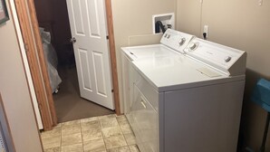 Une buanderie équipée d’un lave-linge et d’un sèche-linge à chargement frontal, d’un sol carrelé et d’une porte donnant sur une autre pièce.