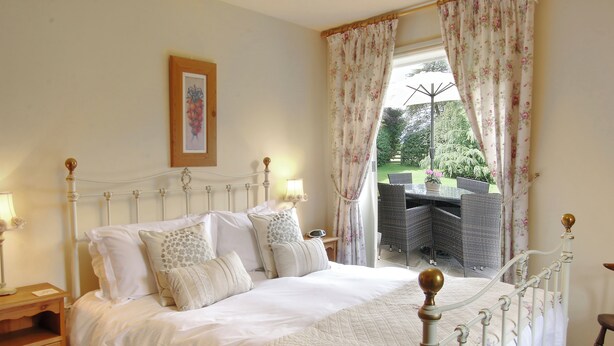 A neatly made bed with a white duvet, a wooden nightstand with a lamp, and a framed picture on the wall. - Beaver Cottage (Thirsk)
