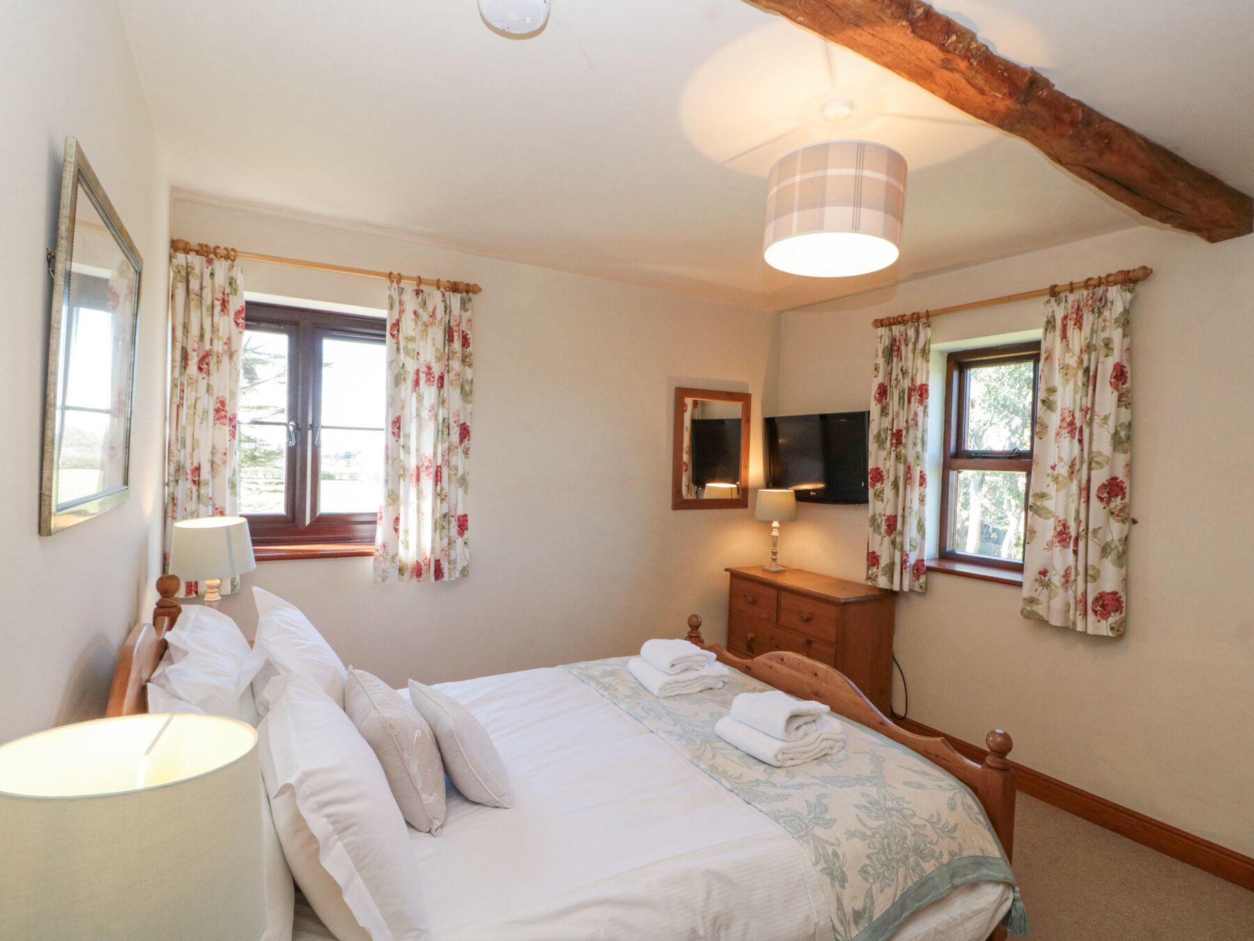 A bedroom with a bed, two bedside lamps, a dresser, a mirror, and a television on the wall.