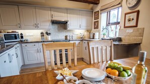 A kitchen with white cabinets, a microwave, and a dining table set with plates, bowls, and a bottle. - Beaver Cottage (Thirsk)