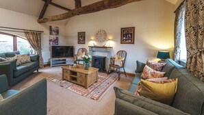 A cozy living room with a fireplace, wooden beams, a television, and comfortable seating. - Beaver Cottage (Thirsk)