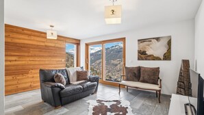 Een moderne woonkamer met een leren bank, een houten accentmuur, een groot raam met uitzicht op bergen, en een hangend kunstwerk.
