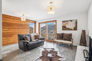 Un soggiorno moderno con un divano in pelle, una parete d'accento in legno, un'ampia finestra con vista sulle montagne e un'opera d'arte appesa al muro.
