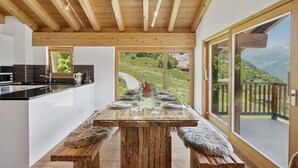 Een moderne keuken met een groot schiereiland, houten balken in het plafond en uitzicht op een bergachtig landschap door grote schuifdeuren van glas.