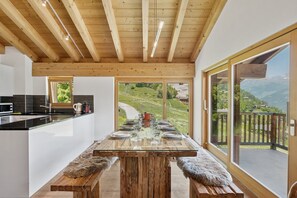 Una cucina moderna con una grande isola, travi in legno al soffitto e vista su un paesaggio montuoso attraverso ampie porte scorrevoli in vetro.
