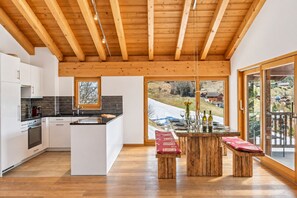 Una cocina moderna con una isla central, vigas de madera en el techo y vistas a un paisaje nevado a través de amplios ventanales.