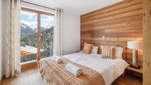 Een slaapkamer met een houten hoofdbord, een groot raam met uitzicht op de bergen, en een bed met twee kussens en een opgerolde handdoek.