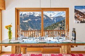 Mesa de comedor preparada para seis personas con vista a la montaña a través de un ventanal grande.
