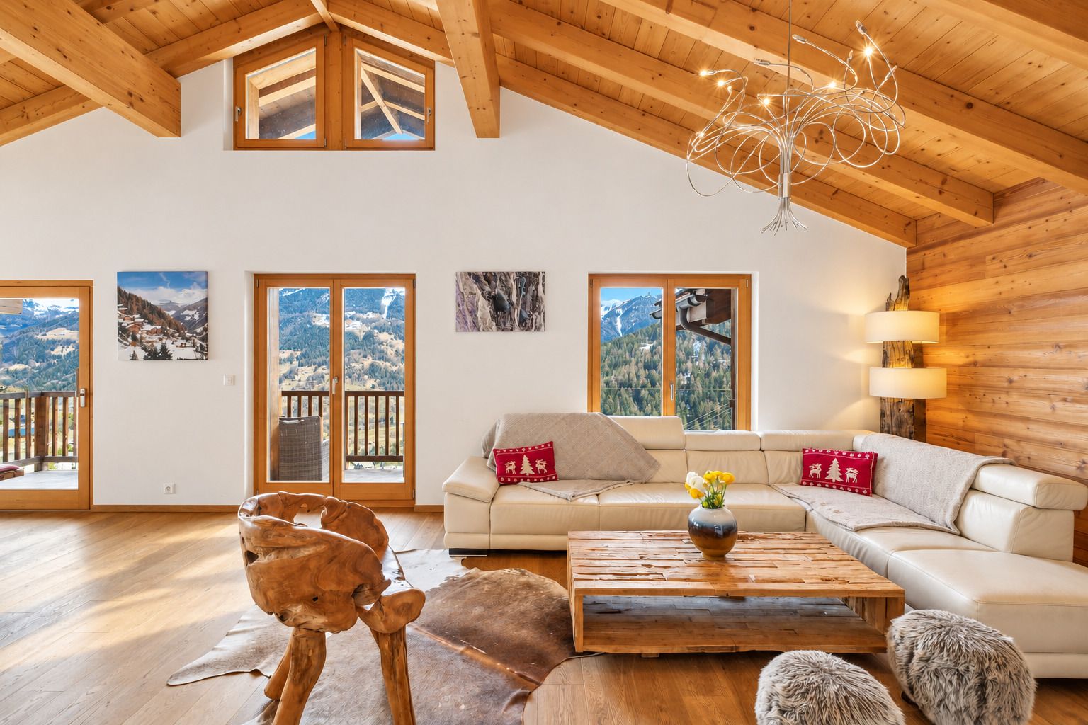 Un salon spacieux avec un plafond haut, des poutres apparentes, un ensemble de canapés, une table basse et une vue sur les montagnes grâce à de grandes fenêtres.