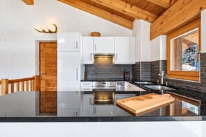 Una cocina moderna con armarios blancos, encimera negra y techo de madera.