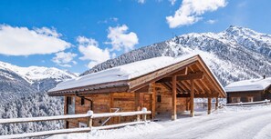 Una cabaña de madera con porche cubierto, rodeada de montañas nevadas.