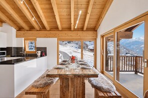Cocina moderna con una isla central, vigas de madera en el techo y grandes ventanales que ofrecen vistas a un paisaje nevado.