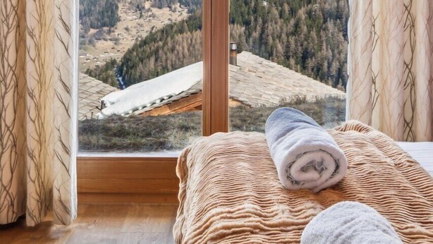 Een slaapkamer met een groot schuifglas dat uitkomt op een uitzicht op bergen.
