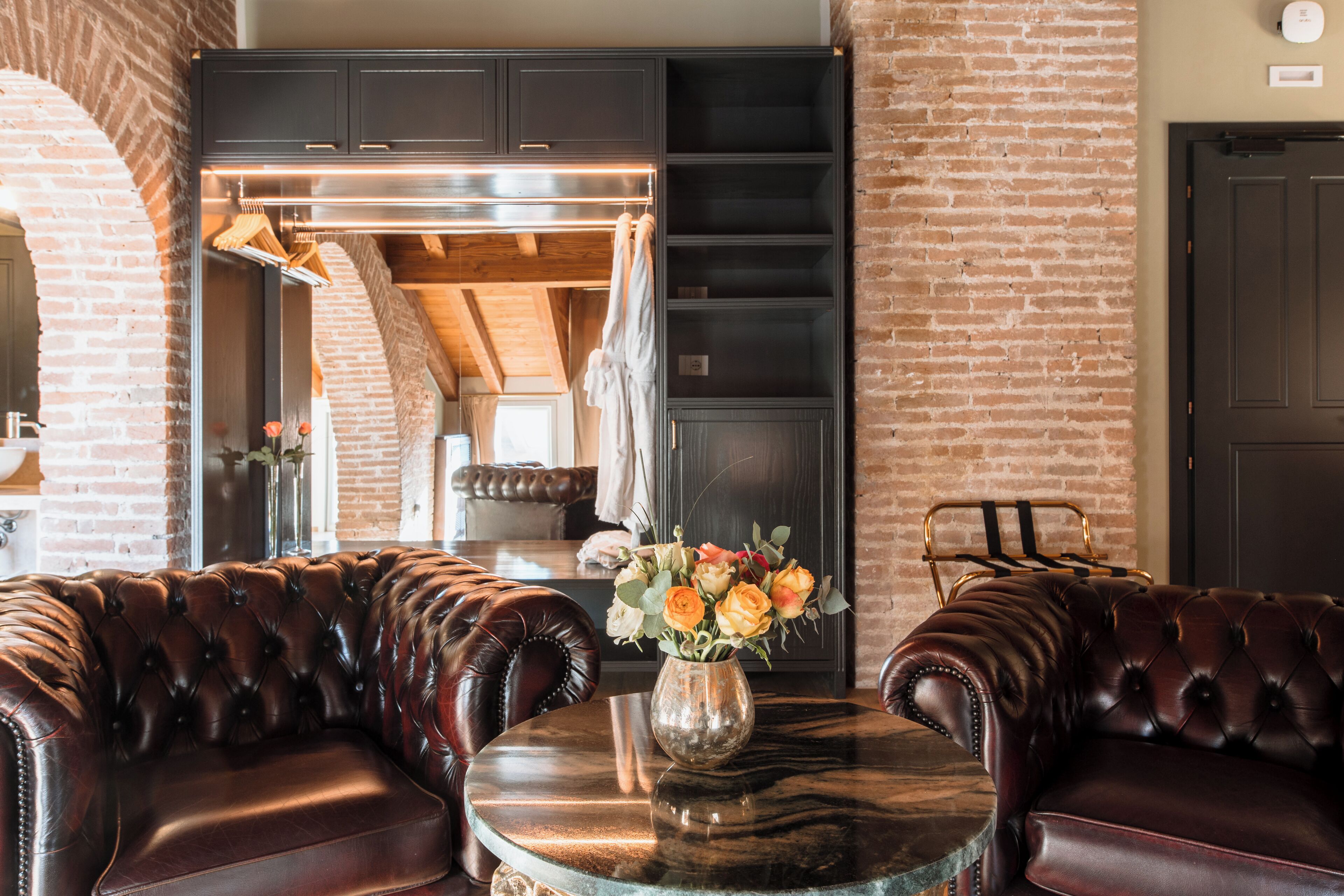 A room with a leather sofa, a marble table with a vase of flowers, and a brick wall.