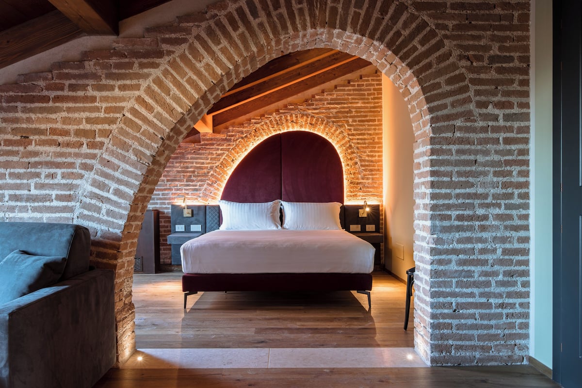 Um quarto com um arco de tijolos, uma cama com roupa de cama branca e um chão de madeira.
