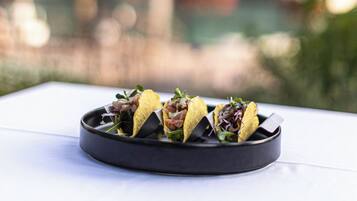 Ein Teller Tacos auf einem Tisch, im Hintergrund eine unscharfe Stadtansicht.