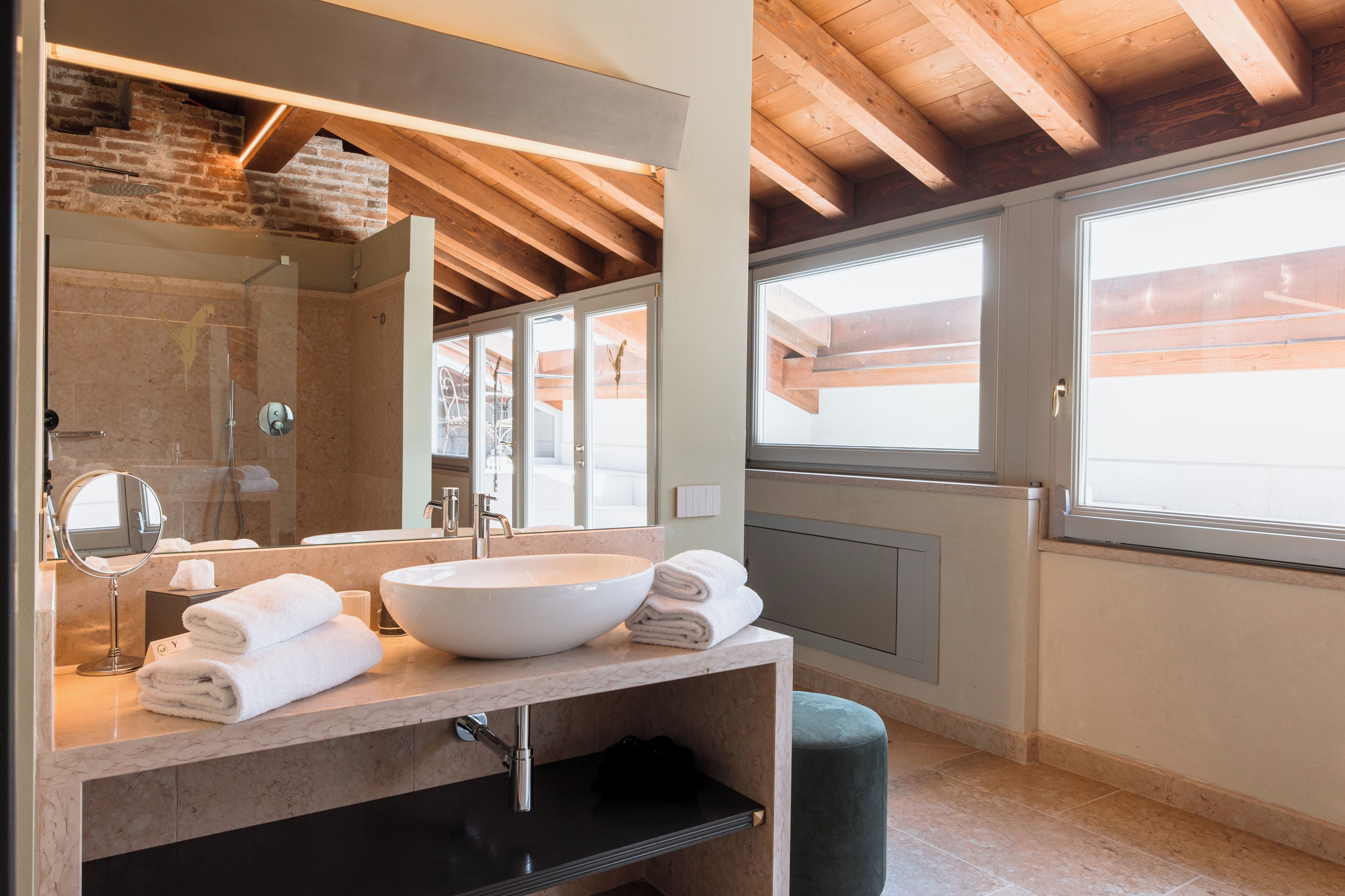 A modern bathroom with a large sink, mirror, and wooden ceiling beams.