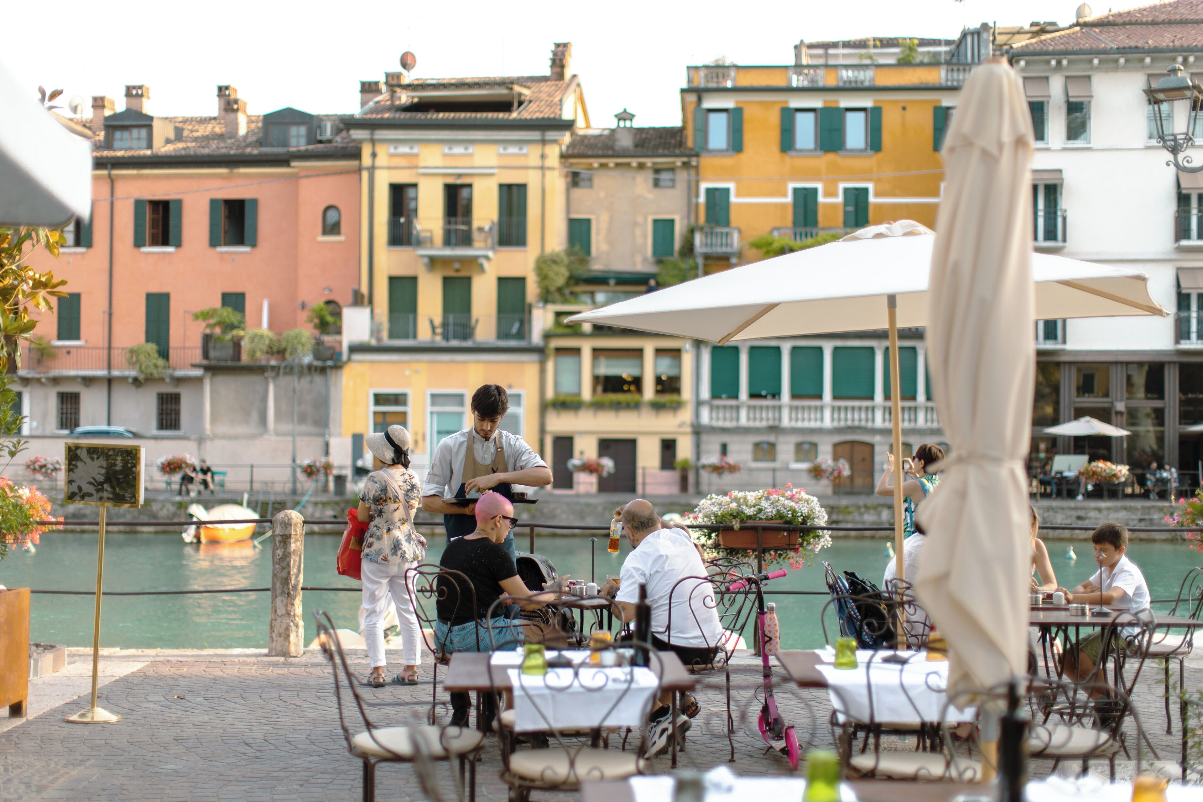 Un restaurant situé au bord de l’eau, avec une terrasse, donnant sur un canal, et avec des bâtiments colorés en arrière-plan.