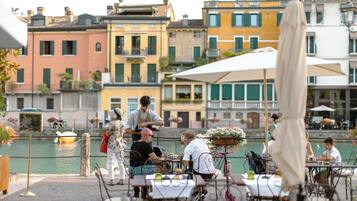 Un restaurant situé au bord de l’eau, avec une terrasse, donnant sur un canal, et avec des bâtiments colorés en arrière-plan.