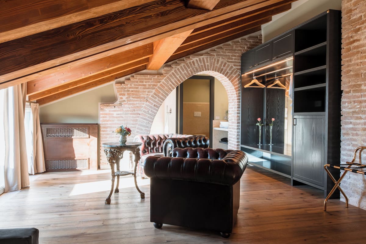 Quarto estilo loft com vigas de madeira aparentes, parede de tijolos e sofá de couro.