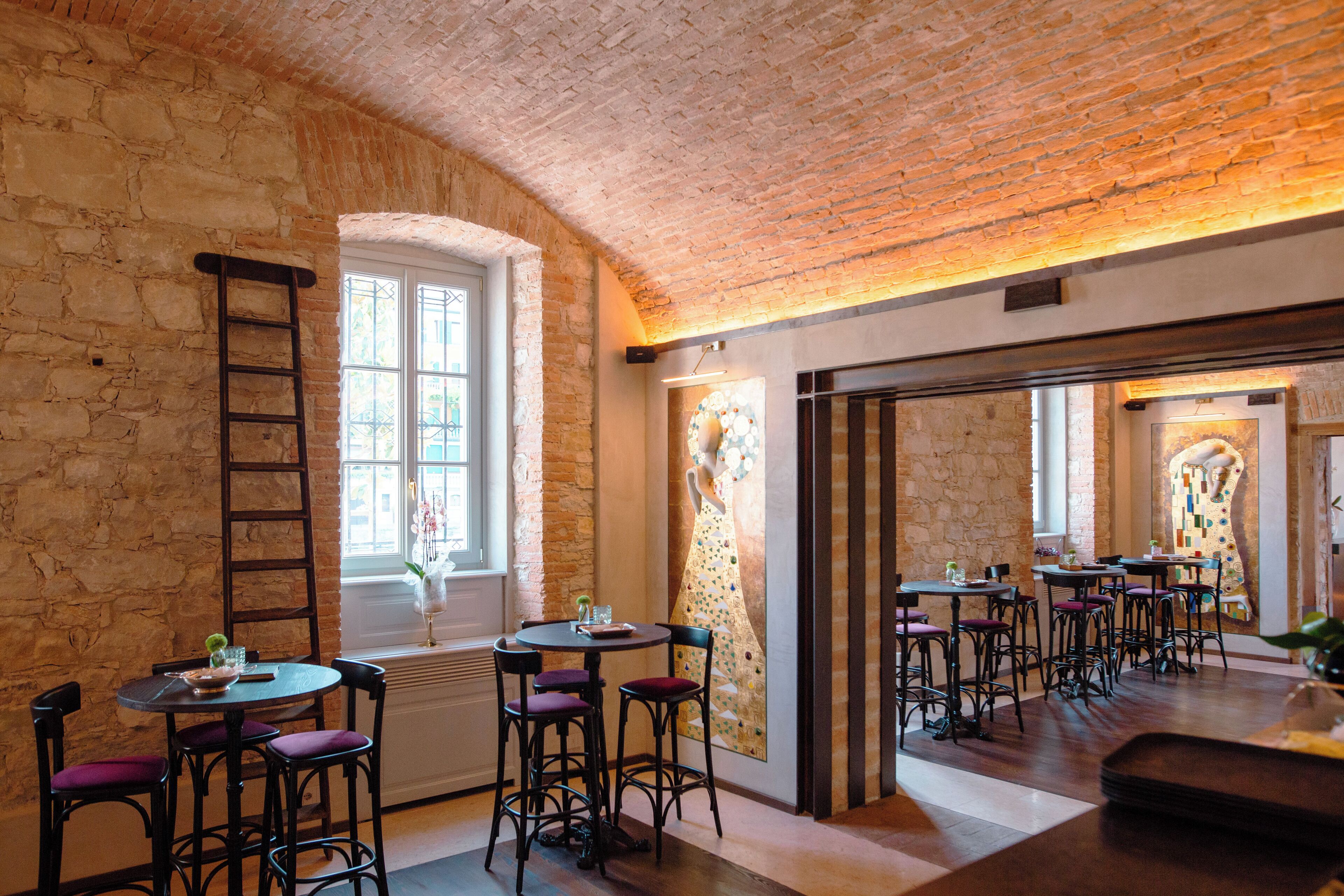 A restaurant with brick walls, a high ceiling, and multiple tables and chairs.