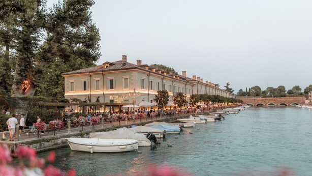 A riverside hotel with a row of boats docked along the water. - Pavillon Suite (Peschiera del Garda)