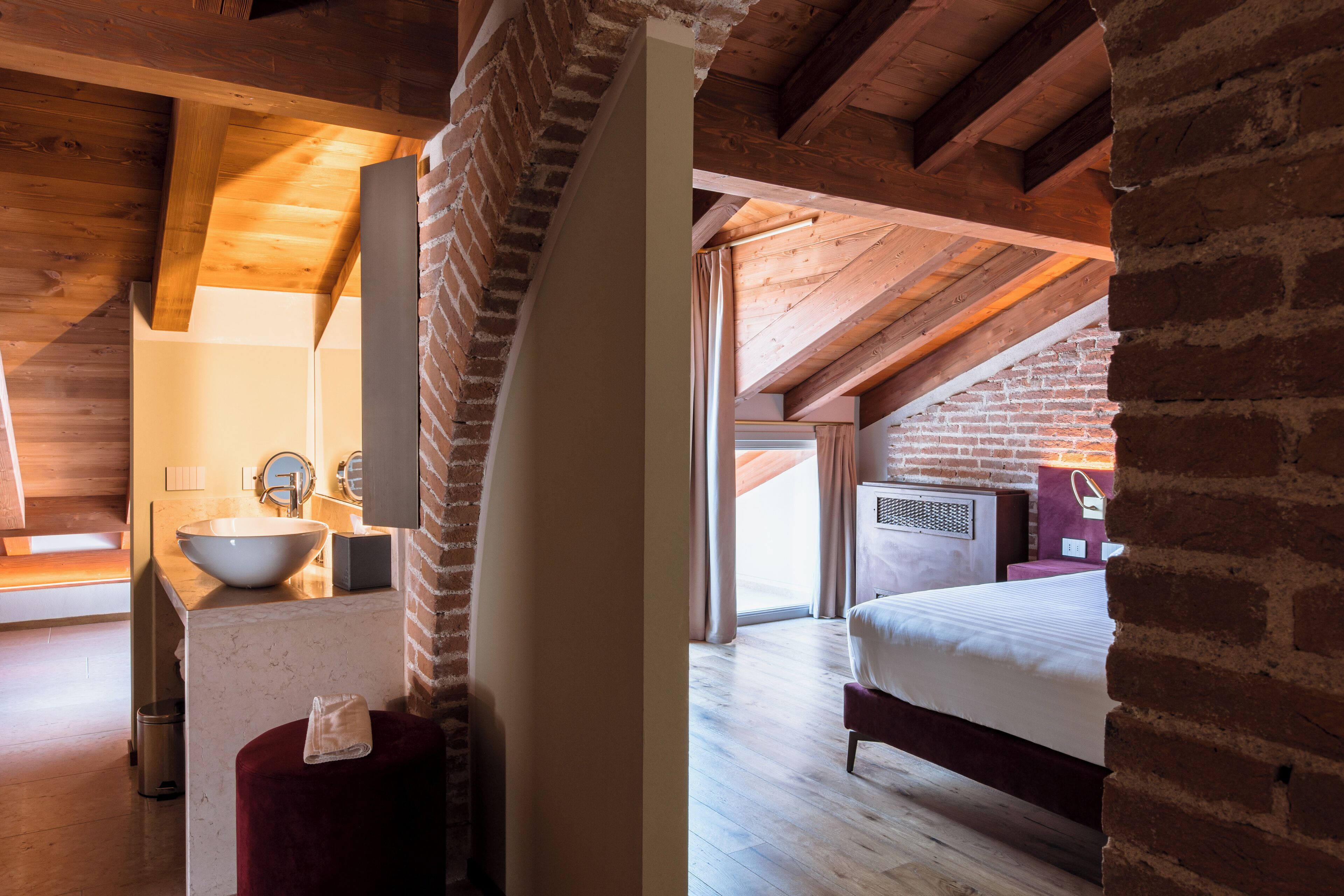 A room with a large bed, a wooden ceiling, and a brick wall.