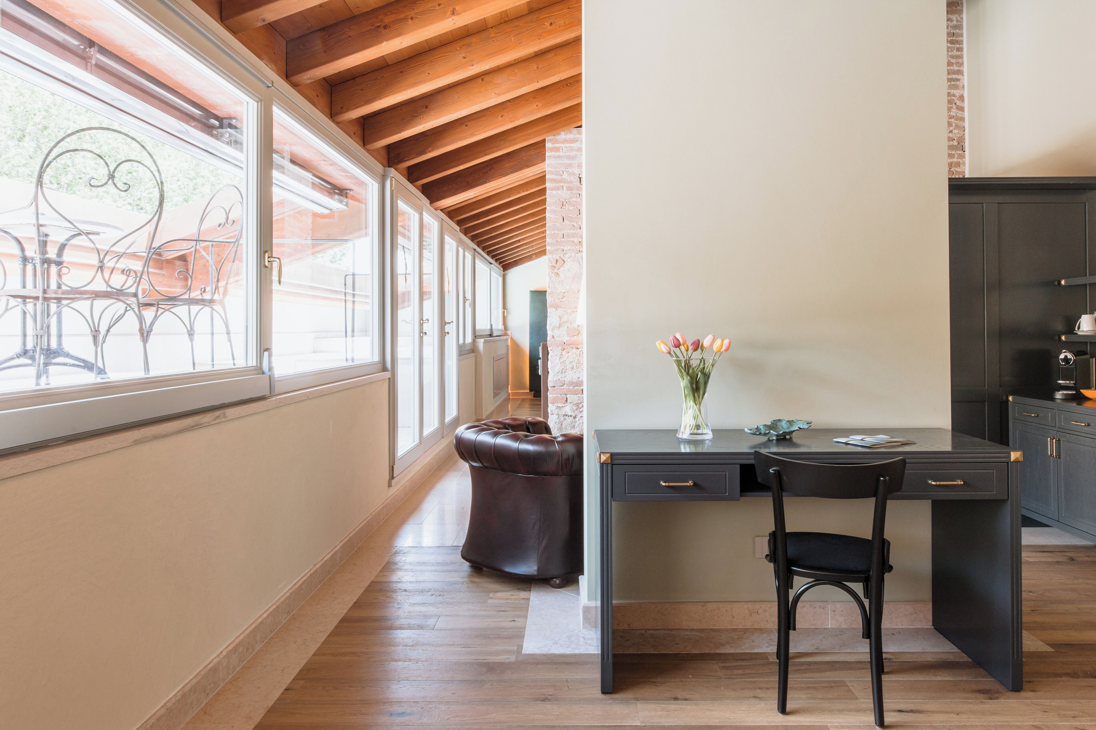 A modern kitchen with a dark countertop, a black chair, and a vase of flowers.