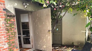 A patio with a brick wall, a door leading to a room, and a tree with pink flowers. - Private cottage close to SoFi, FiFa fans welcome! (Long Beach)