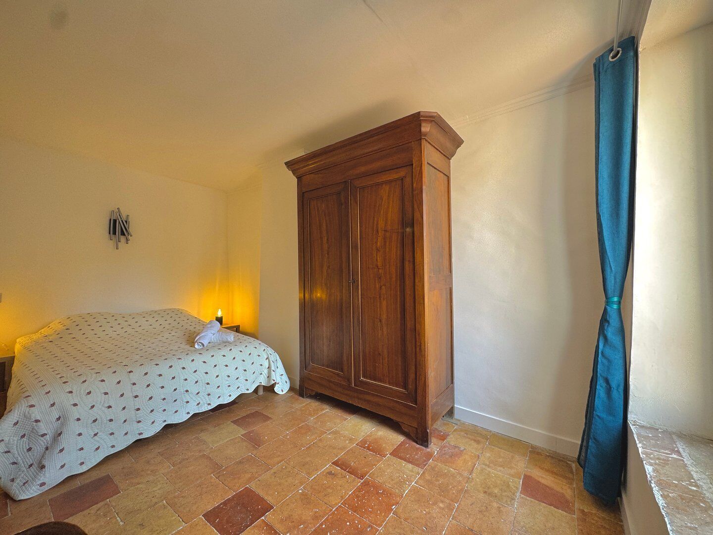 A bedroom with a bed, a wooden wardrobe, a nightstand, and a blue curtain.
