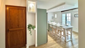 A modern kitchen with a wooden door, a white island with bar stools, and a view of the dining area.