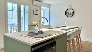 A modern kitchen with a built-in dishwasher, a large island with a sink, and a dining area with chairs and a table set for four.