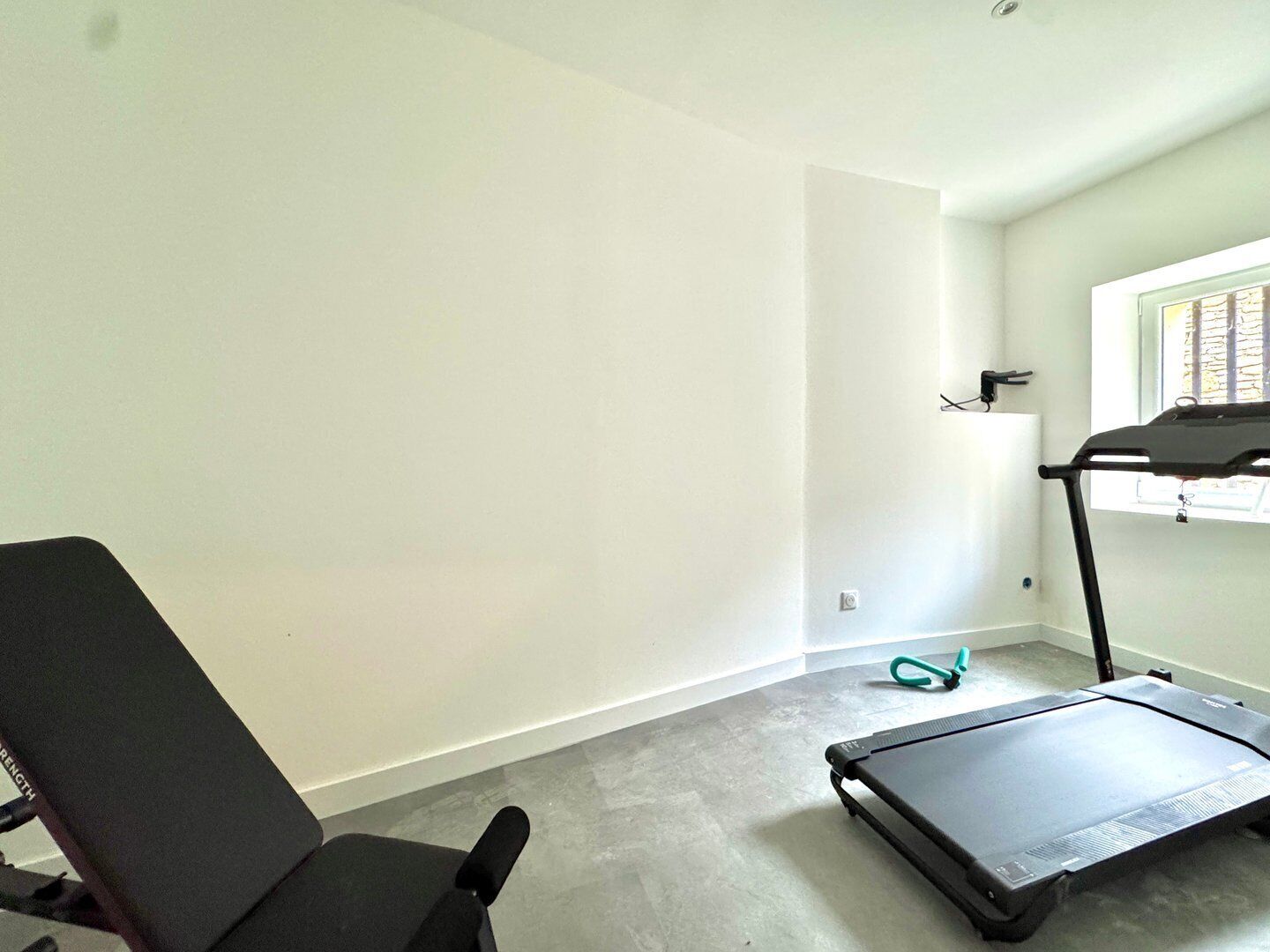 A room with a treadmill, a black exercise chair, and a window with blinds.