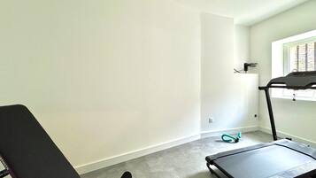 A room with a treadmill, a black exercise chair, and a window with blinds.