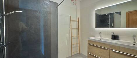 A modern bathroom with a shower, a wooden ladder, a large mirror, and a vanity with drawers.