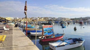 A marina with boats docked, a pier with benches, and a cityscape in the background.