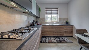 A modern kitchen with a gas stove, wooden cabinets, a window with blinds, and a kitchen mat.