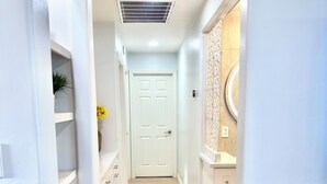 Un pasillo con una puerta blanca al final, piso de madera y paredes blancas.