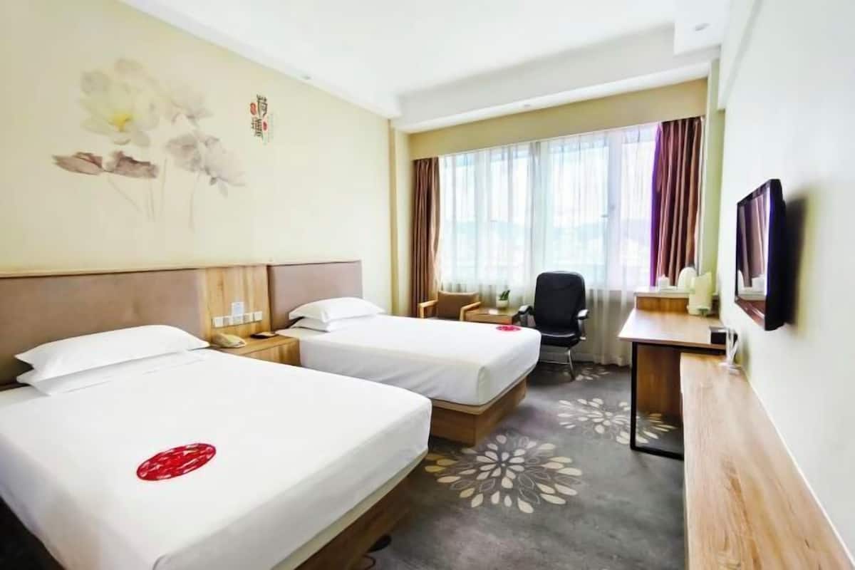 Une chambre d’hôtel avec deux lits, un bureau, une chaise, une télévision et une fenêtre avec des rideaux.