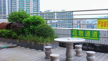 Una terraza en la azotea con una mesa redonda y taburetes, rodeada de vegetación y vistas a rascacielos.