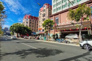 Un hotel de fachada roja, con un cartel que dice 'Longyan Landscape Hotel' y un estacionamiento con coches y bicicletas.