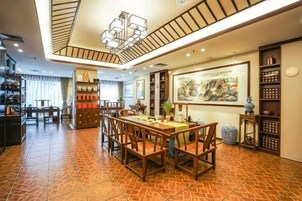 Un comedor de hotel con una mesa y sillas de madera, una lámpara en el techo y una estantería con libros.