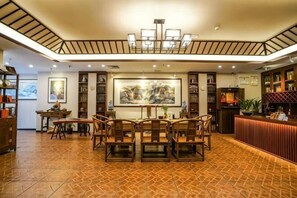 Un restaurante con una mesa central rodeada de sillas, un cuadro grande en la pared y un mostrador de recepción.