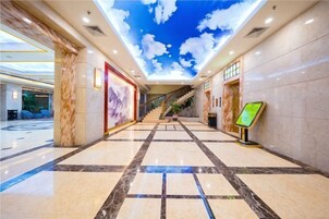 Un hall de hotel con piso de mármol, una escalera y un techo con diseño de nubes.