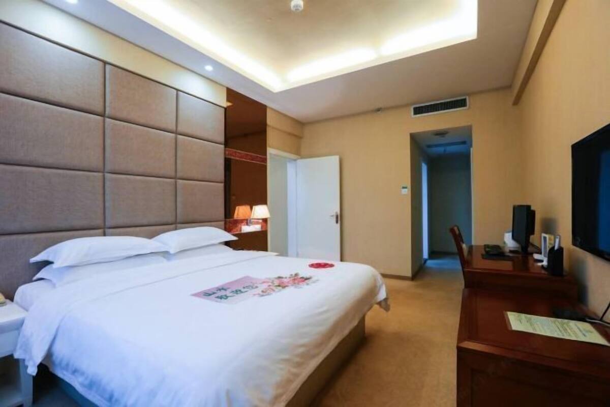 Une chambre d’hôtel comprenant un lit, une table de chevet, une lampe, un bureau, une chaise et un téléviseur.
