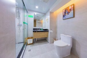 Un baño moderno con cabina de ducha de vidrio, tocador de madera y un inodoro blanco.