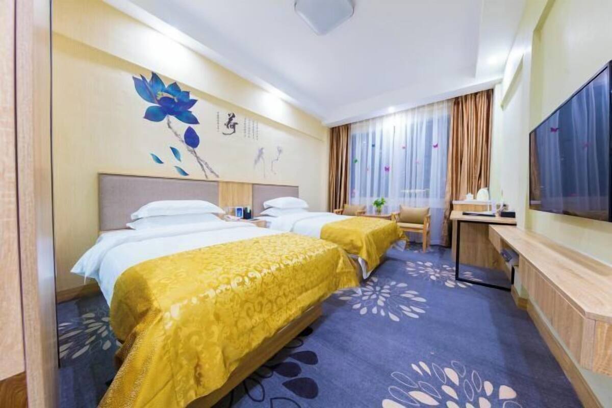 Une chambre d’hôtel avec deux lits, un bureau, une télévision et une fenêtre avec des rideaux.