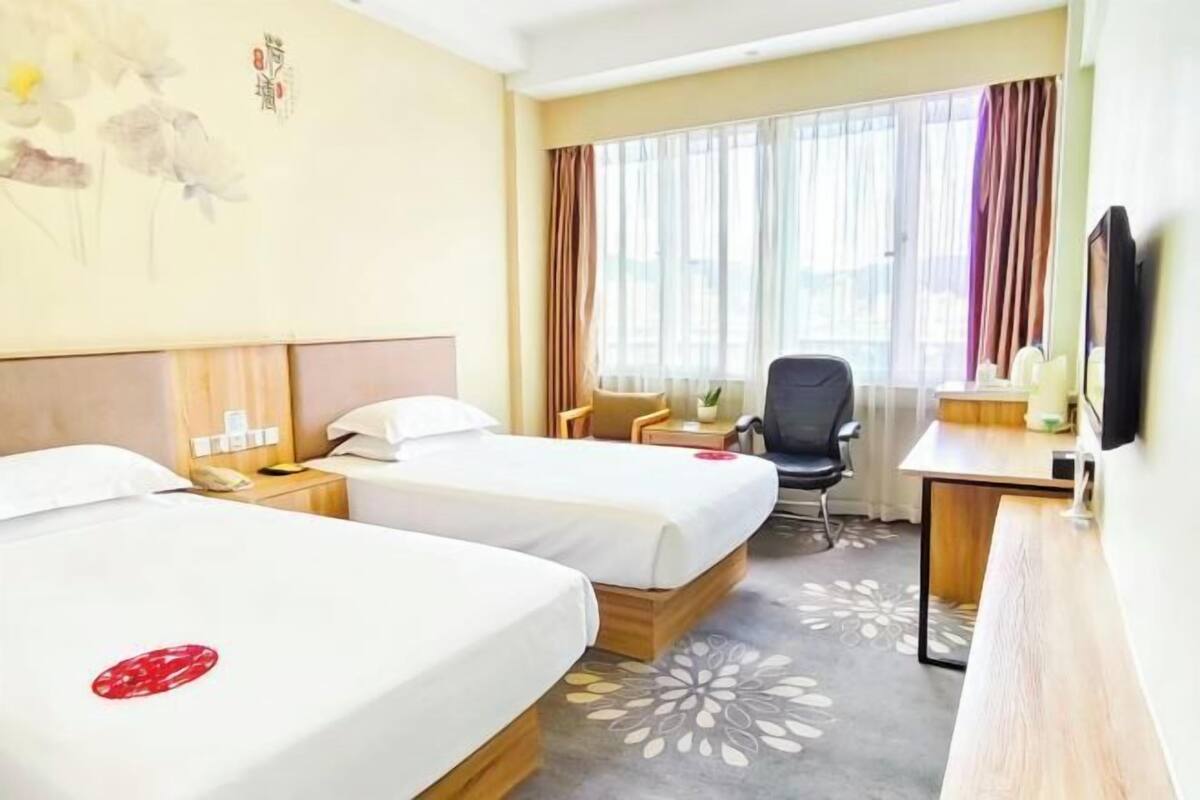Une chambre d’hôtel avec deux lits, un bureau, une chaise, une télévision et une fenêtre avec des rideaux.