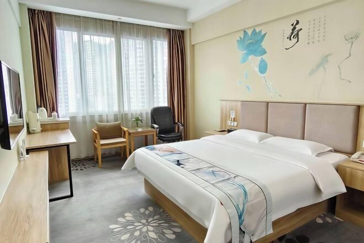 Une chambre d’hôtel avec un lit, un bureau, une chaise, une télévision et une fenêtre avec des rideaux.